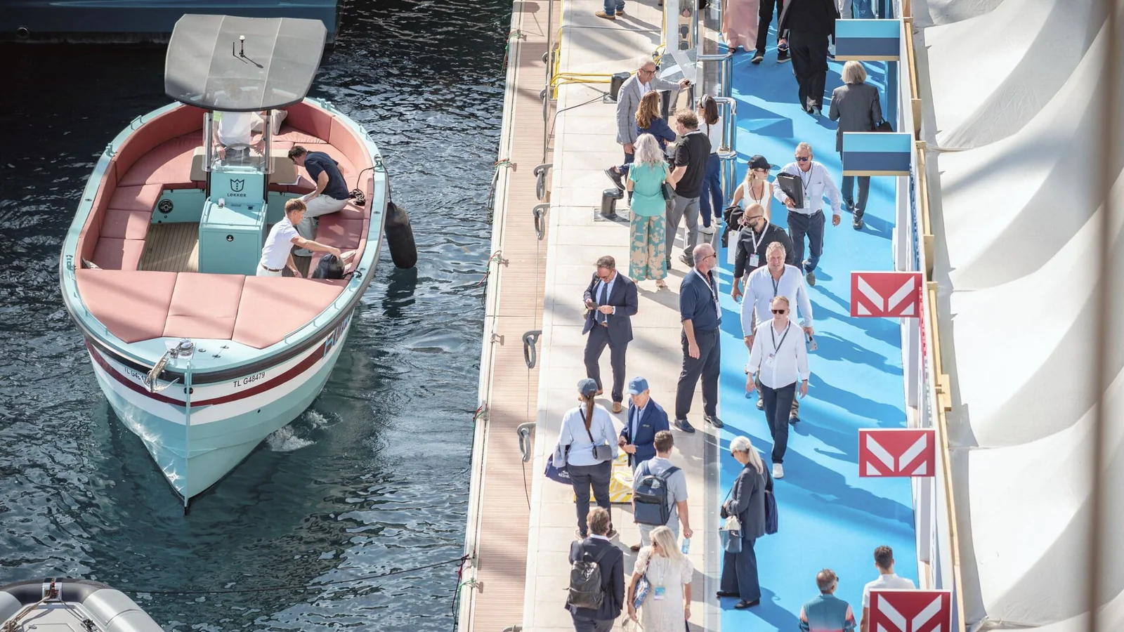 Odwiedzający w strefie Dockside podczas Monaco Yacht Show, obok zacumowanych superjachtów